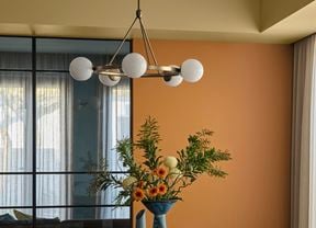 A feature wall painted in Dulux Magic Melon, with windows draped by curtains, a feature pendant light and a vase of flowers in the same colour scheme.