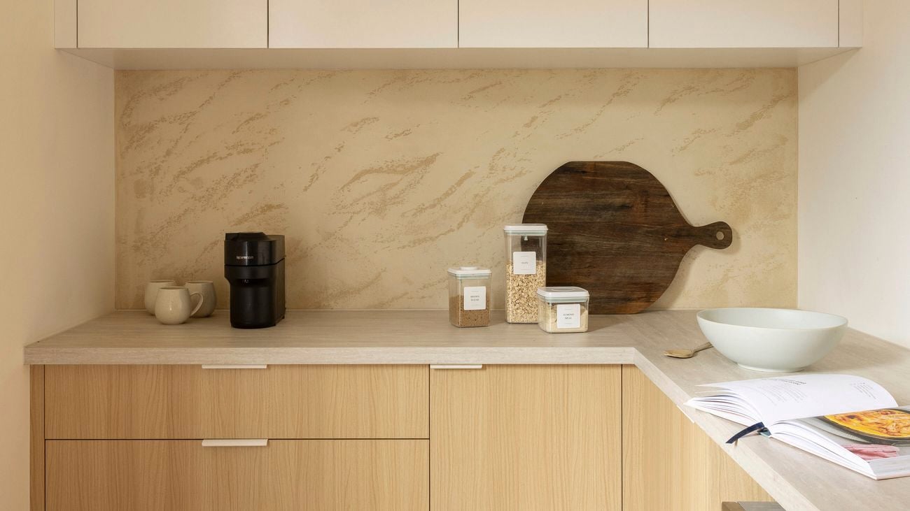 A modern kitchen with light wood-look cabinets and benchtops, and a patterned splashback.