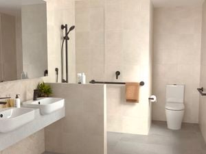 Modern beige bathroom with a toilet, 2 basin's, shower and a hand rail attached to the wall.