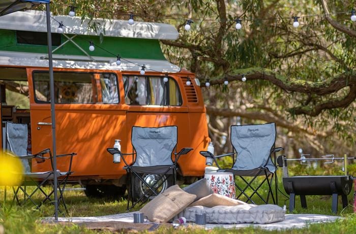 Orange combi van with camp chairs, outdoor cushions, outdoor lights and rugs.