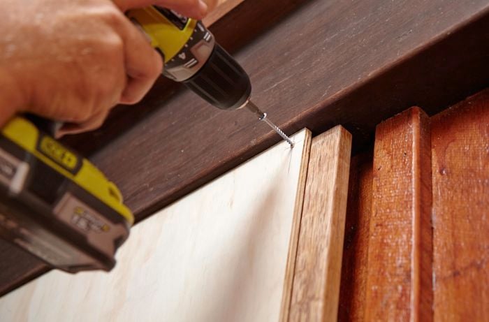 Plywood panels being screwed into a window frame with a power drill