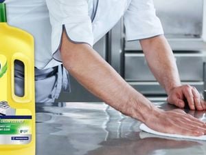 A man’s arms cleaning a stainless steel kitchen bench with a bottle of Jif cream cleanser in the foreground