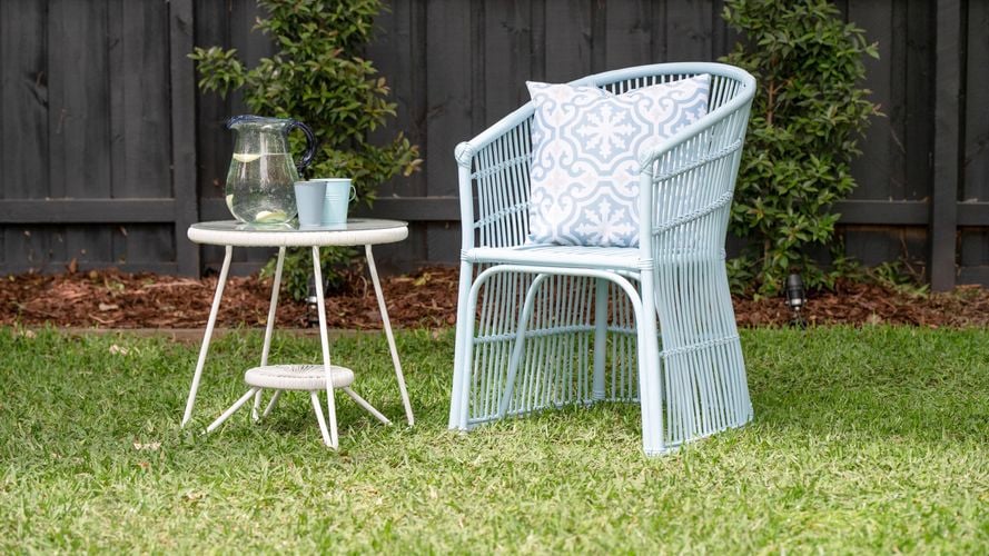 Complete painted wicker chair styled with a small outdoor coffee table on a lawn