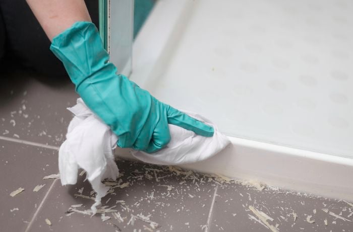 A hand in green gloves is cleaning the surface with a cloth, and there is silicone residue scattered on the floor.