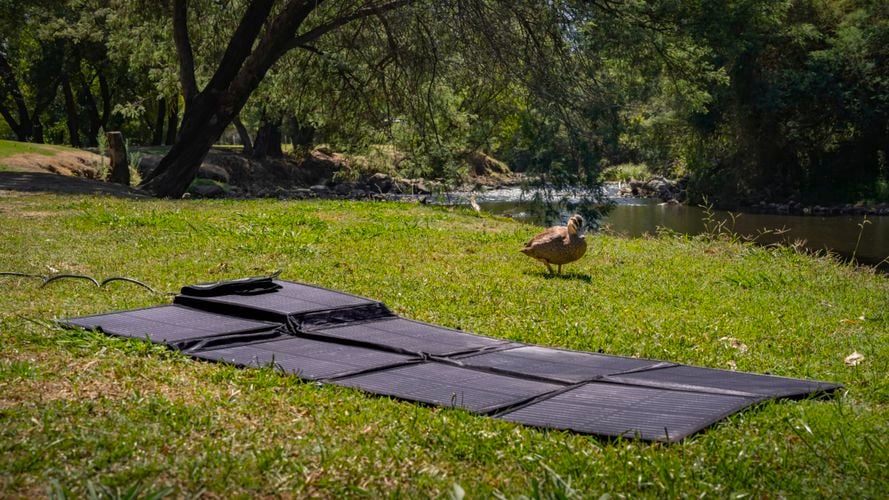 KT Solar 300W Solar Folding Blanket laid out on grass beside a river at a campsite.