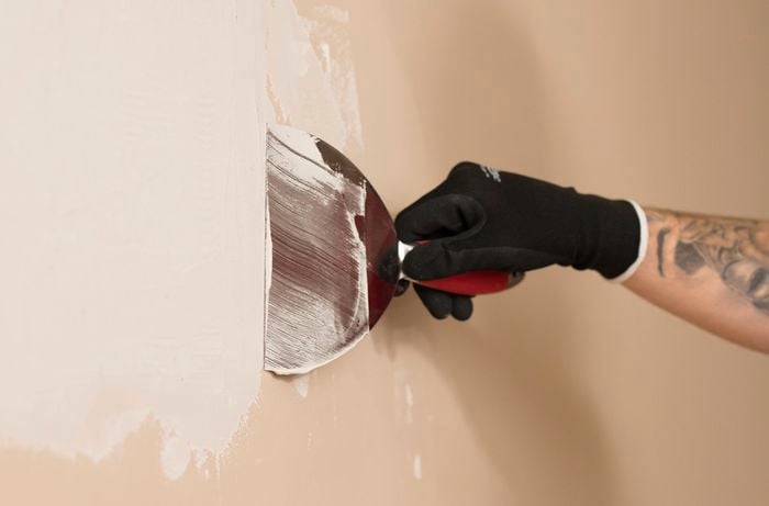 A gloved hand is using a trowel to spread the base coat evenly over the plasterboard.
