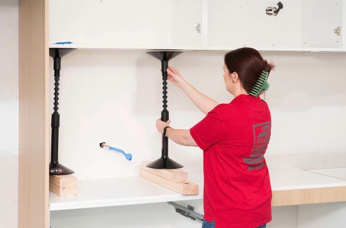 A Bunnings Team Member is using cabinet support to hold overhead cabinets in place during installation.