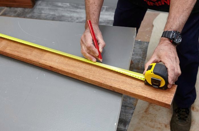 Person using measuring tape and making a mark on piece of timber with pencil.