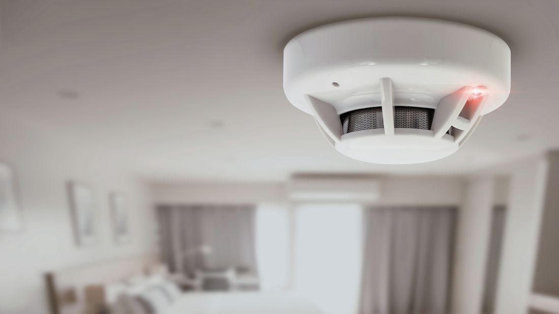 Smoke alarm attached to ceiling with red light on.