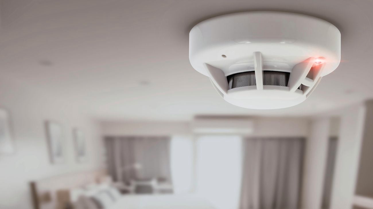 Smoke alarm attached to ceiling with red light on.