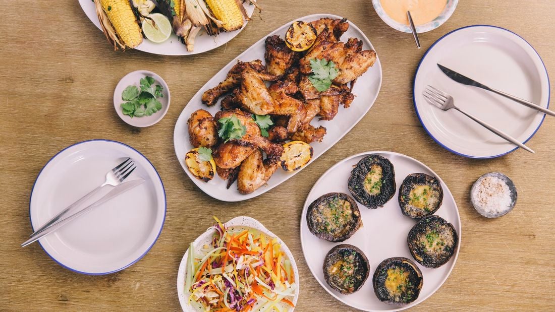 A plate of cooked chicken on a table with barbequed corn and mushrooms