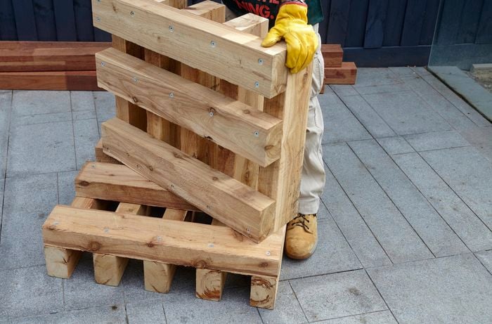 Two completed ends of a wooden outdoor day bed being held up by a Bunnings team member