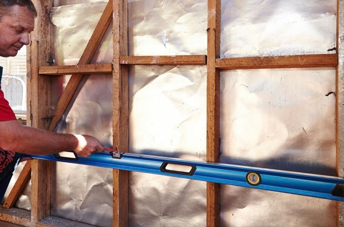 A person marking measurements on wall studs using a spirit level