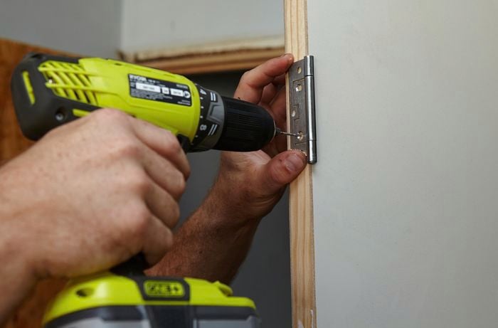 Holes being drilled into a door frame for screws, using a door hinge as a guide