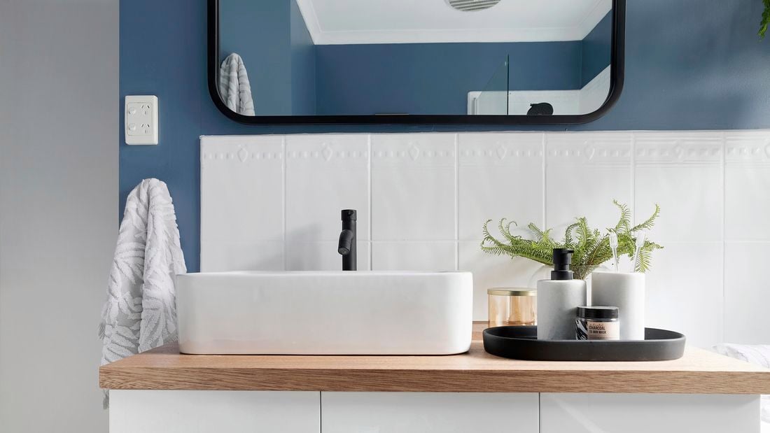A stylish black mixer tap in a modern white bathroom with vanity and plants.