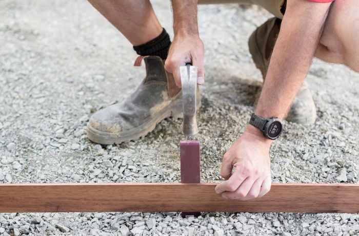 Person hammering in an edging peg next to a length of timber edging on a gravel base.
