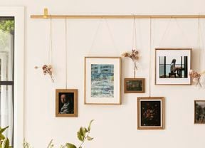 D.I.Y. hanging artworks and floral arrangements designed as a gallery wall from a gold rod on a cream wall behind a table