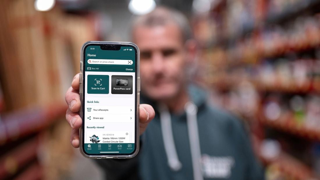A close-up of a man’s hand holding a phone that shows the Bunnings Trade PowerPass app in use
