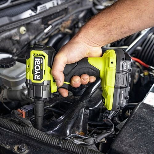 A person using an impact wrench to tighten bolts on a car engine.