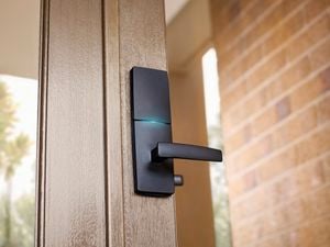Close up of a black Gainsborough smart lock installed in a wooden-framed glass front door.