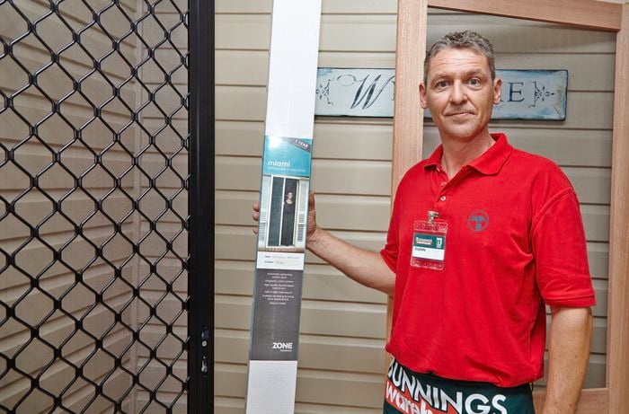 Bunnings team member Glen holding a retractable screen door in packaging