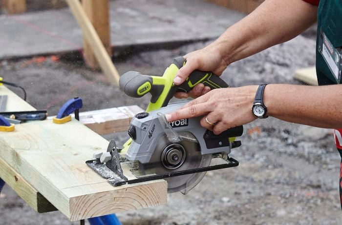 A person using a circular saw to cut a length of timber