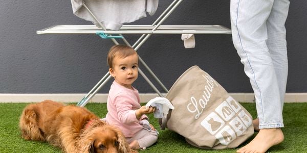A toddler with a dog and a laundry bag sitting on turf grass.