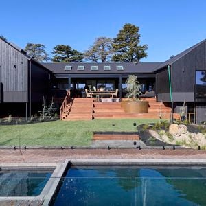 The back of a house with a pool in it, a rocked area, timber decking and many plants in it.