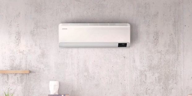 An air conditioner set into a stone wall in front of a double bed