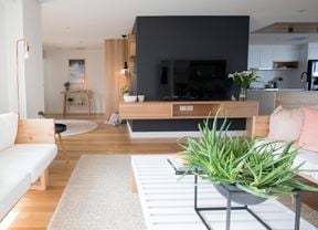 Modern living room area with black feature wall, timber floors and accents and cream couches.