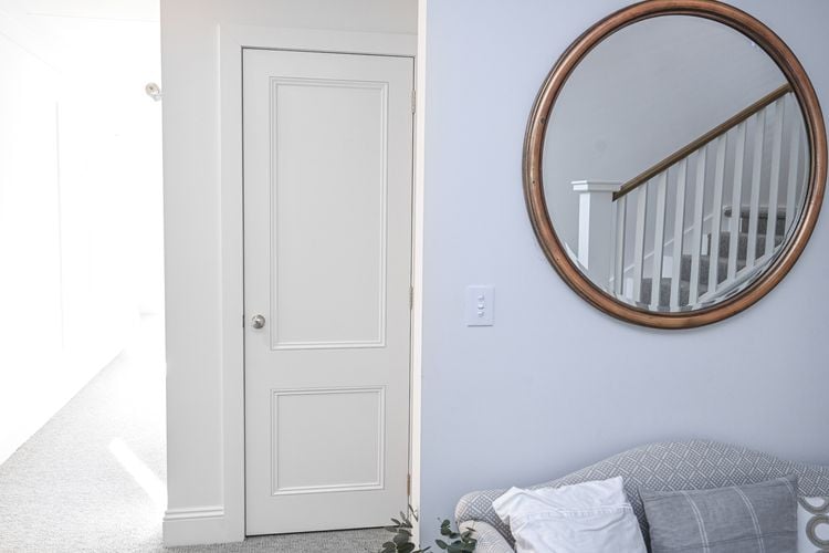 Lounge room with grey couch, large circular mirror and white wooden door