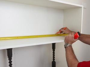 Person marking inside a wall mounted cabinet using a measuring tape and pencil