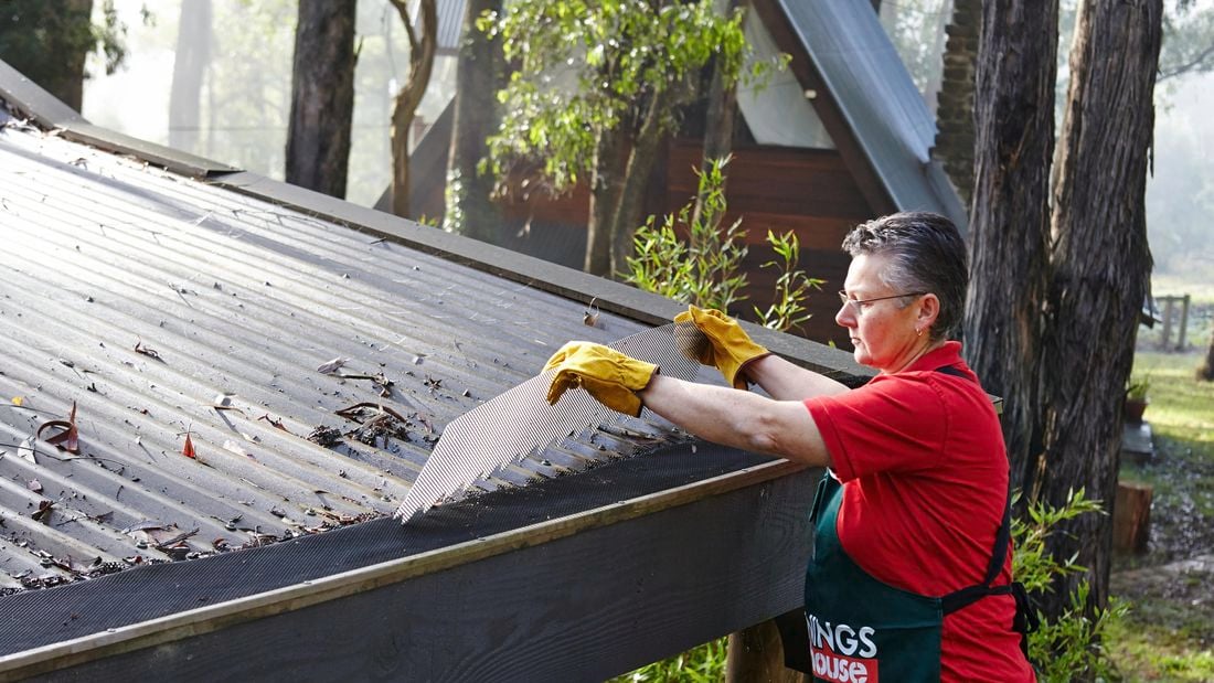 Person fitting gutter guard to a roof in a bushland setting