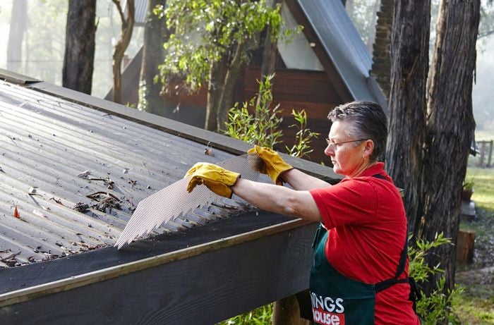 Person fitting gutter guard to a roof in a bushland setting