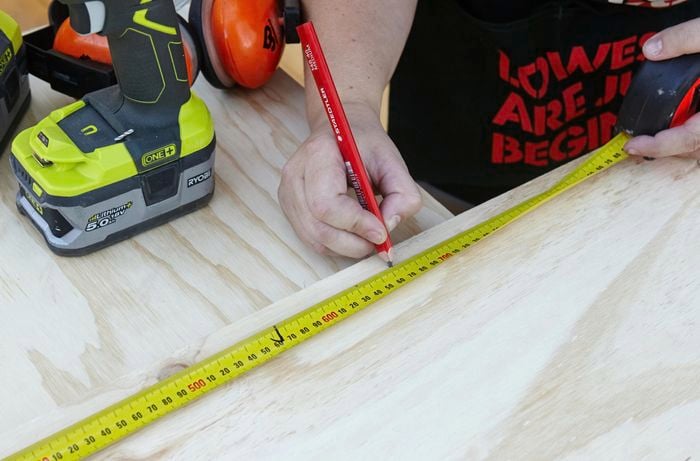 A pencil and tape measure being used to mark a panel of wood
