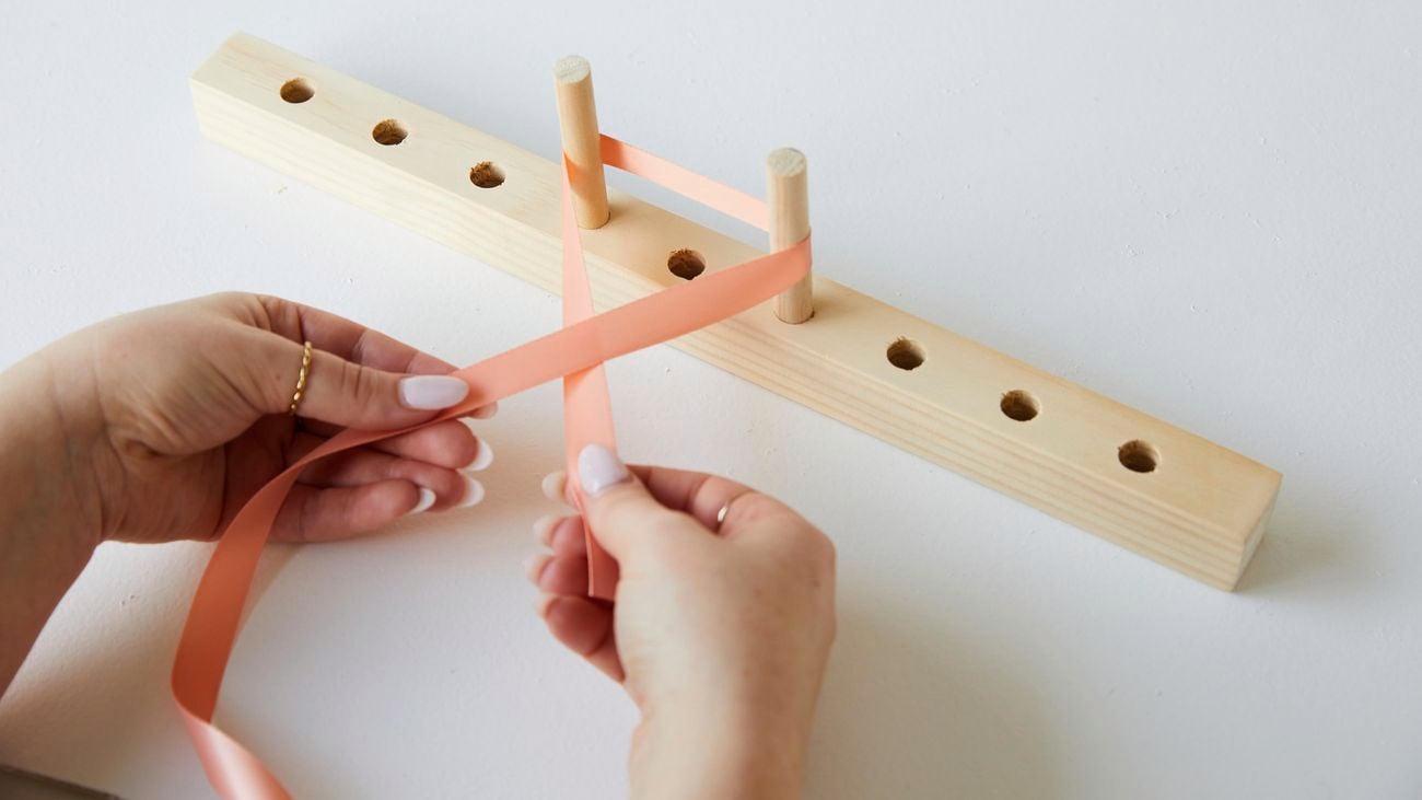 A person using a bow maker to create a bow from peach coloured ribbon.