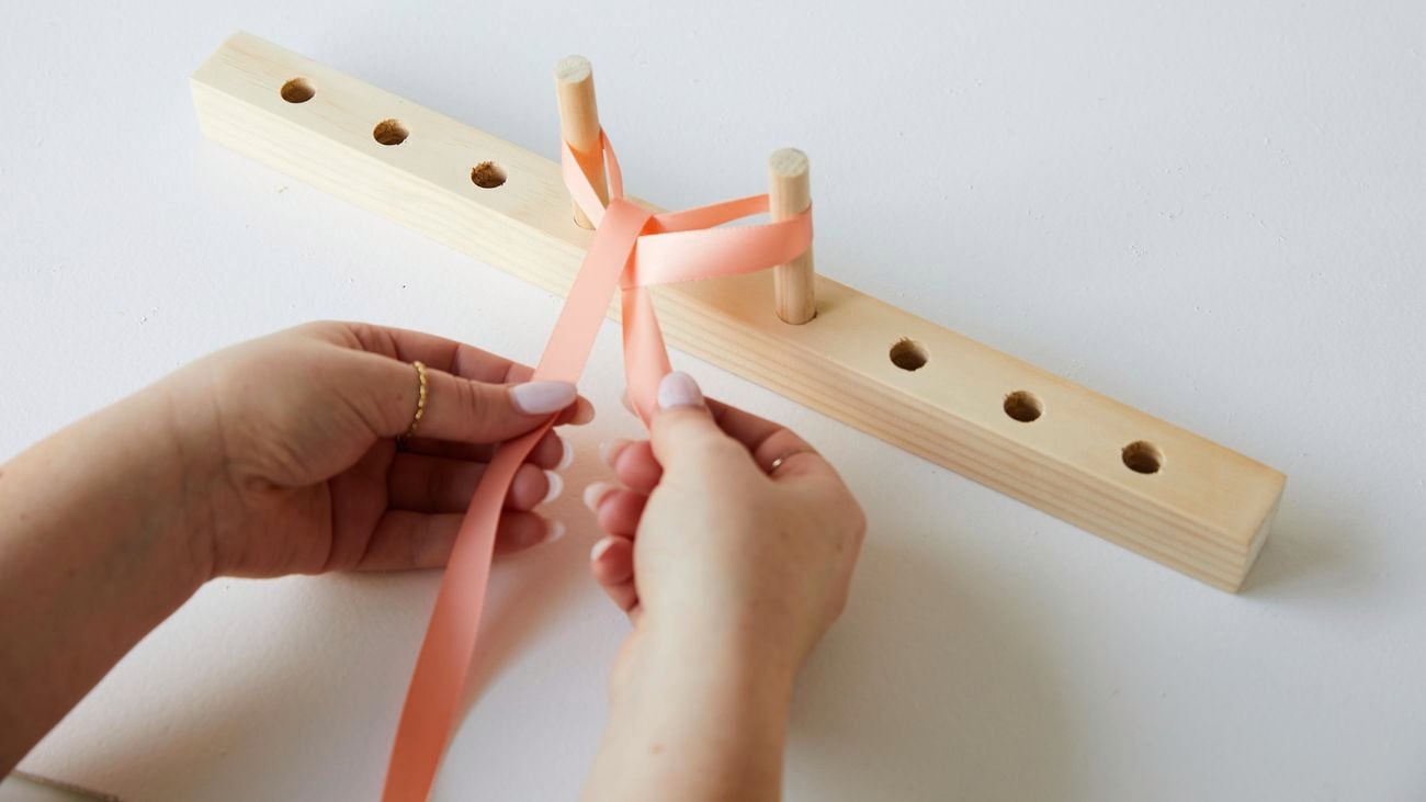 A person using a bow maker to create a bow from peach coloured ribbon.