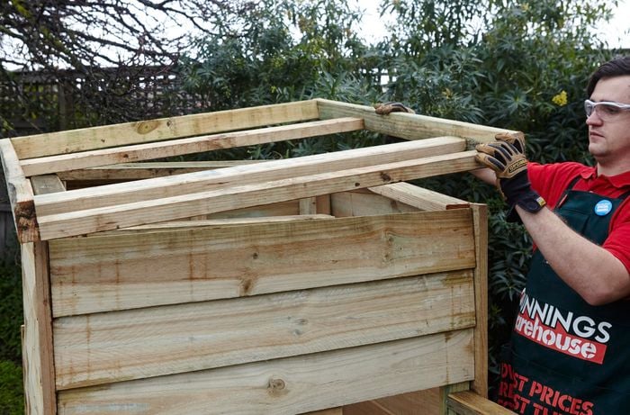 A roof frame being lowered onto a chicken coop by a Bunnings team member