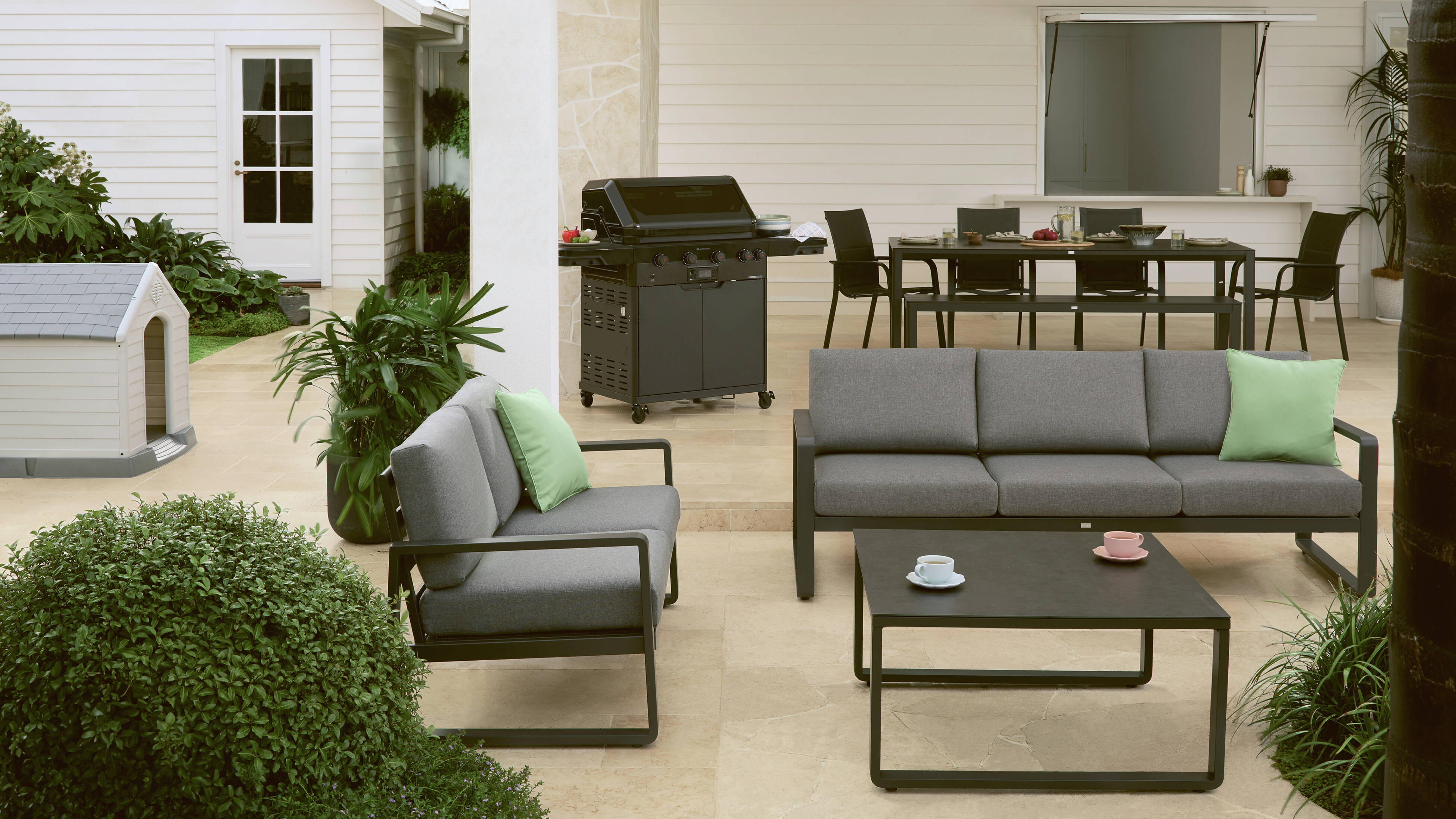 Outdoor living area with grey sofa, black coffee table, dining set, and BBQ