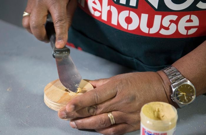 A person filling a hole in a plywood circle using wood filler