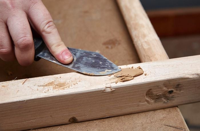 Person using putty and spatula to cover up major indents on DIY wooden ladder.
