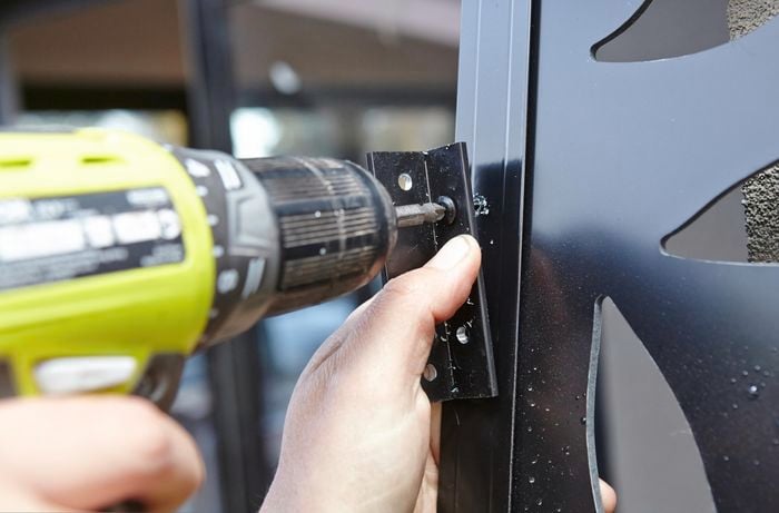 A bracket being screwed to a metal screen with a cordless drill