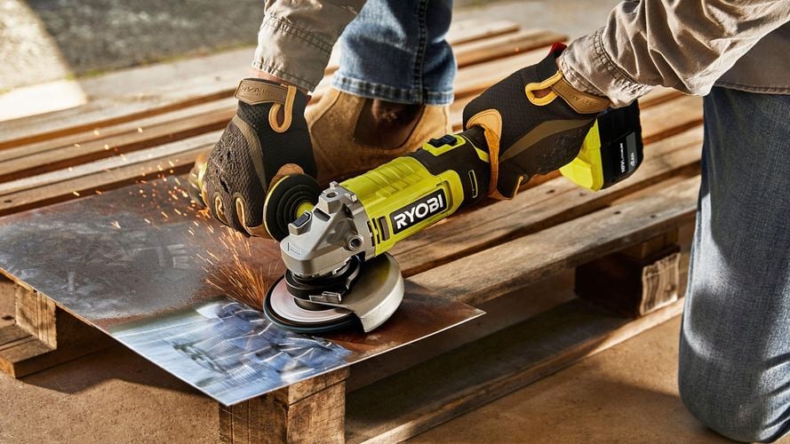 A person using a handheld grinder to smooth and shape a piece of metal on pallet.
