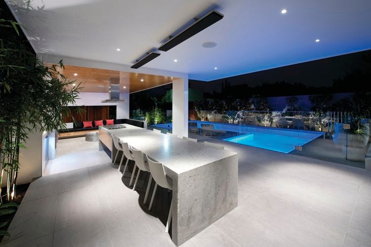 A stone outdoor dining area near a pool with roof mounted heat lamps