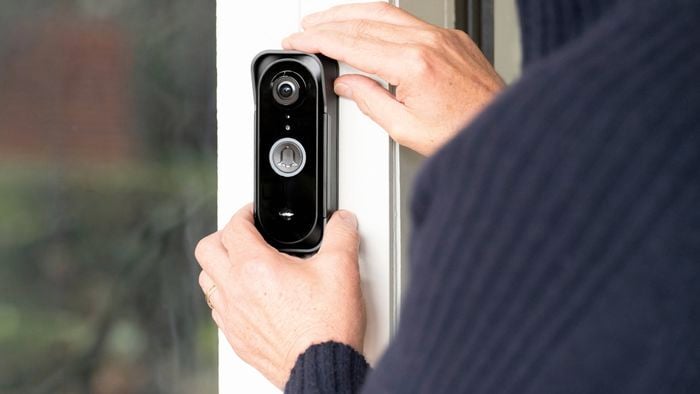 A person with their hands on a smart ring doorbell attached to a piece of painted timber.