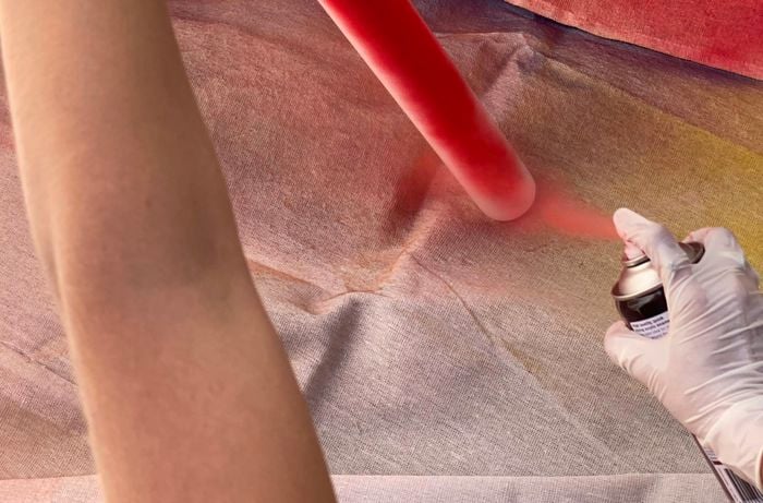 A gloved pair of hands spray painting a PVC pipe