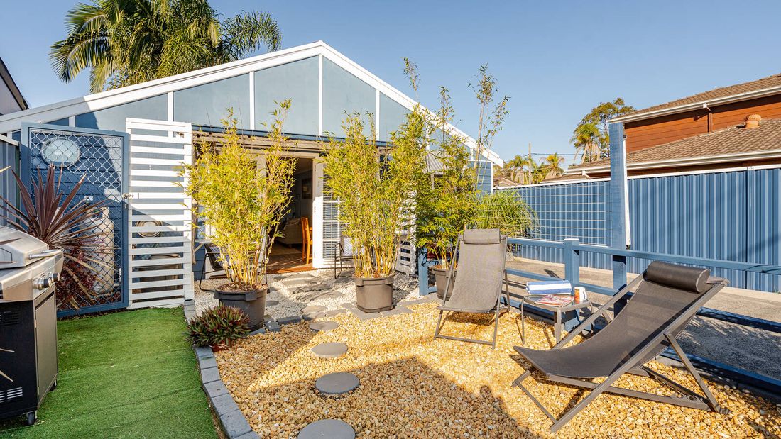 Exterior view of a small blue cottage with white trim, double glass doors, potted bamboo and outdoor seating.