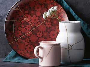 A cup, vase, and flower-patterned plate repaired with kintsugi techniques, each with a vein of gold running through
