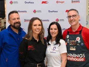Bunnings team member and employees with corporate uniforms in front of a board with logos.