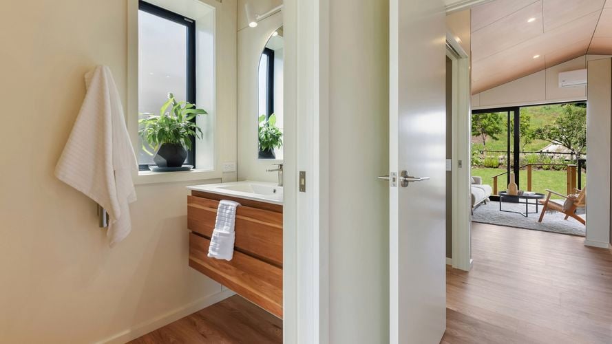 Bathroom vanity with timber cabinet, mirror and frosted window, opening to living area beyond.